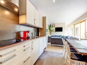 Una cocina moderna con una cafetera roja, un comedor con mesa y sillas, y una sala de estar con sofá y televisor.