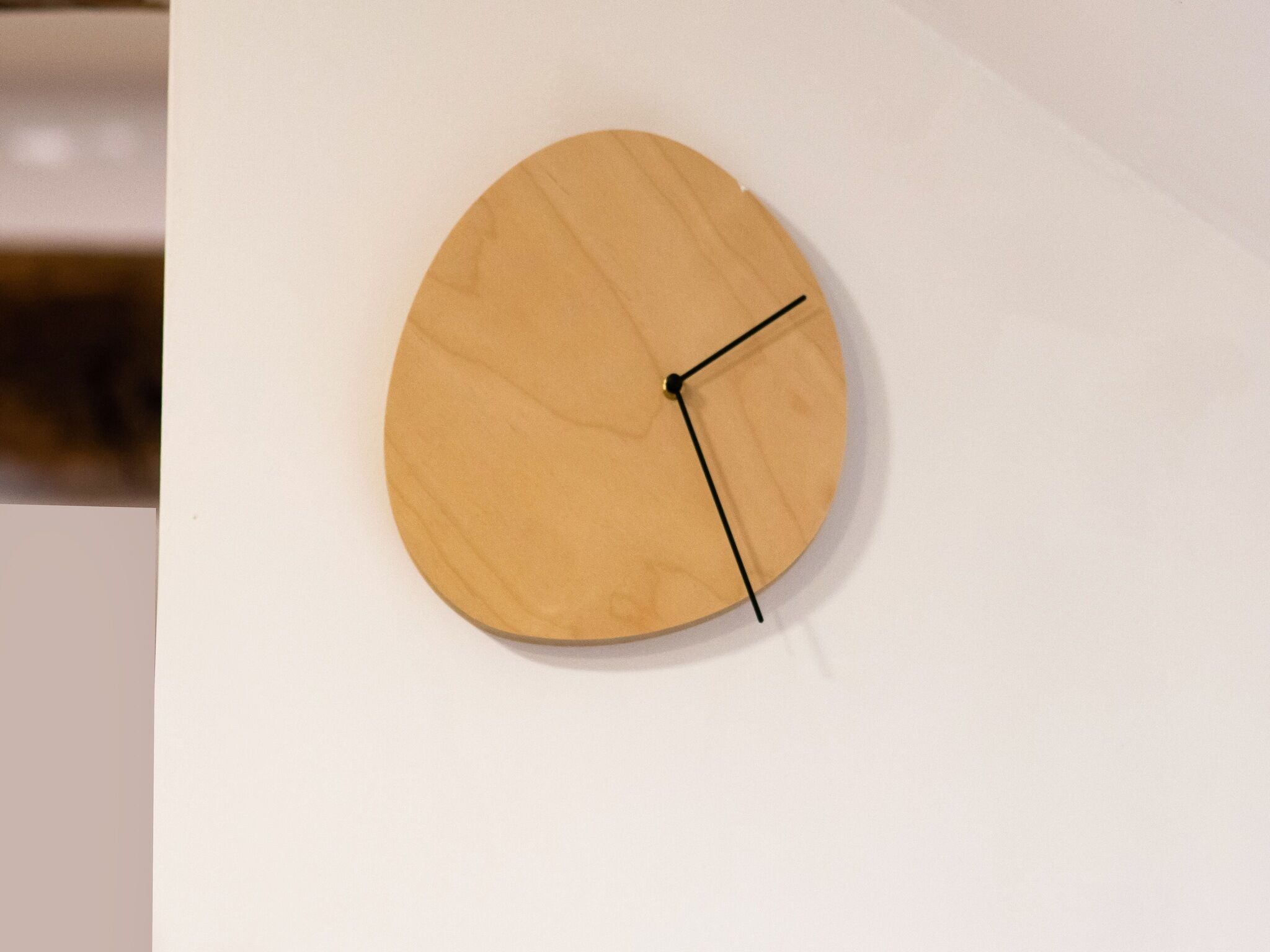 A round wooden clock with a minimalist design, mounted on a plain white wall.