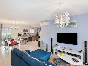 A modern living room with a sectional sofa, a flat-screen TV, and a dining area with a kitchen in the background.