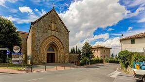 Una iglesia de piedra con una entrada de arco apuntado, una torre de campanas y un letrero de estacionamiento cerca.