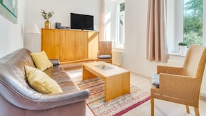 A modern living room with a leather sofa, a wooden coffee table, a wicker armchair, and a television on a wooden cabinet.