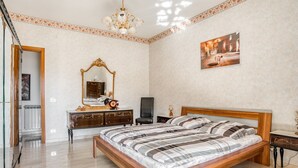 A bedroom with a large bed, a wooden headboard, a mirror, a dresser, and a chandelier.