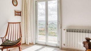 A room with a wooden rocking chair, a large sliding glass door leading to a balcony, and a radiator on the wall.