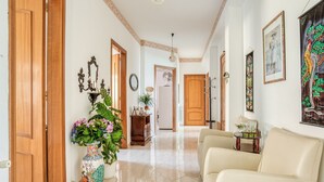 A hallway with a beige sofa, a large vase with flowers, and a wooden door.
