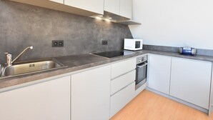 Uma cozinha moderna com pia de aço inoxidável, armários brancos, micro-ondas e forno embutido.