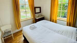 A hotel room with a bed, a chair, a nightstand, and a window with curtains.