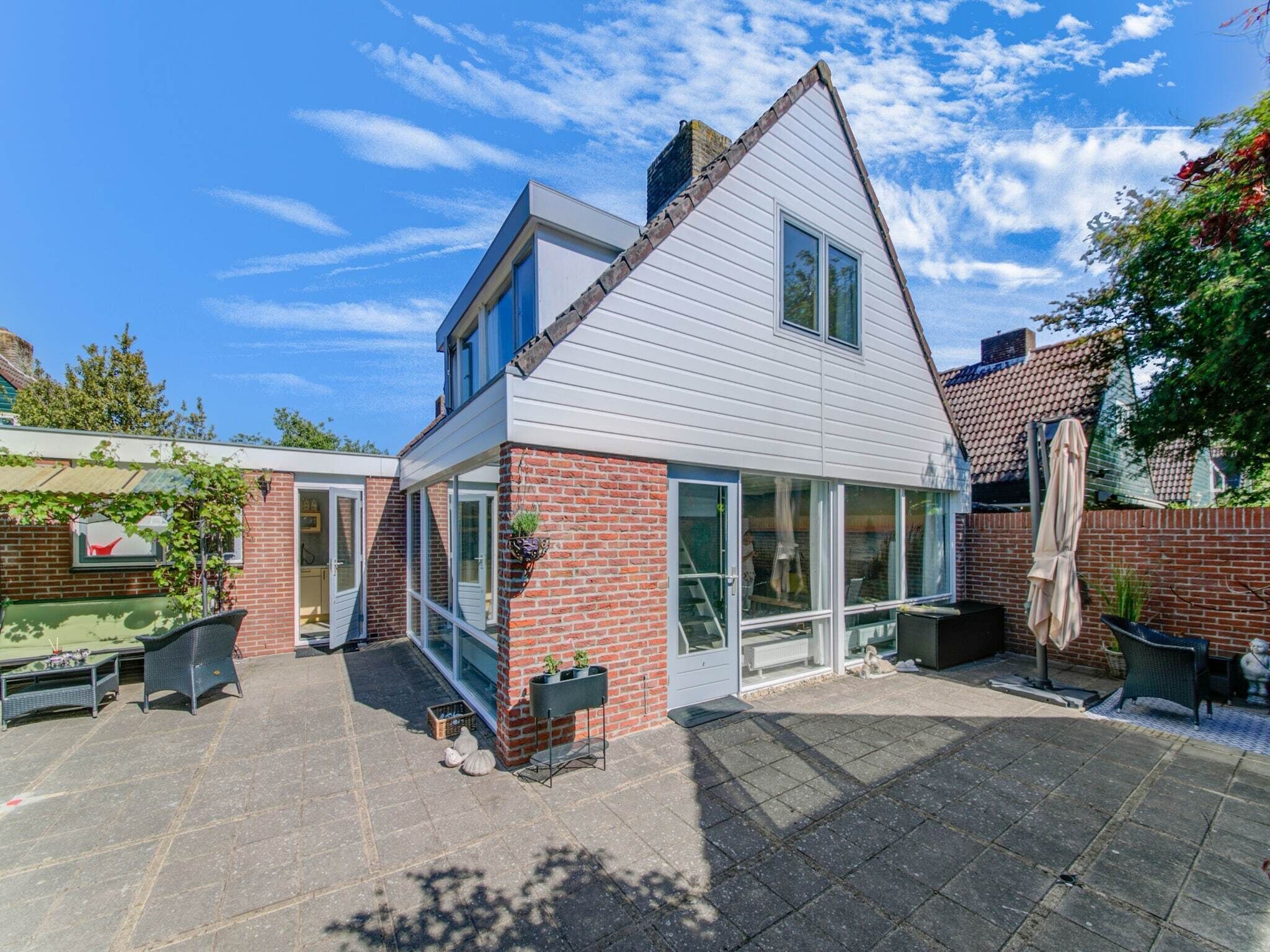 A two-story house with a brick facade, large windows, and a patio area with outdoor furniture.
