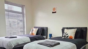 Ein Doppelzimmer mit zwei Betten, jeweils mit Kopfstütze, und einem Fenster mit Jalousien.