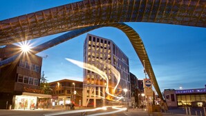 Ein modernes Gebäude mit einer gewölbten Fassade und einer großen, beleuchteten Bogenkonstruktion darüber.