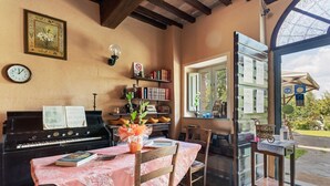 Una habitación acogedora con un piano, una mesa de comedor con mantel floral y una estantería.