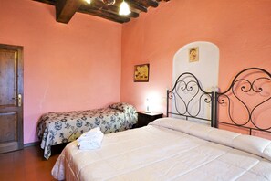 Quarto com duas camas, porta de madeira, mesa de cabeceira com abajur e um quadro na parede.