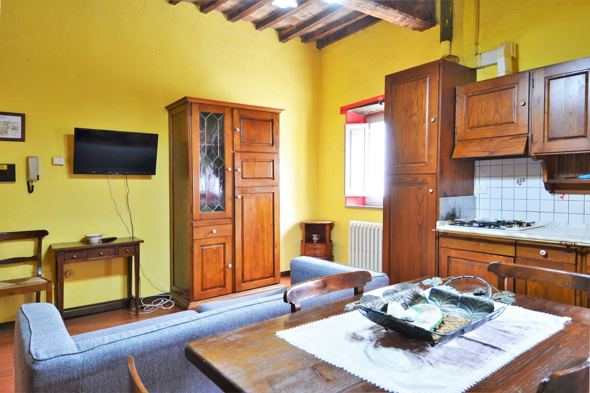 A compact kitchen with wooden cabinets, a dining table with a placemat, and a television mounted on the wall.