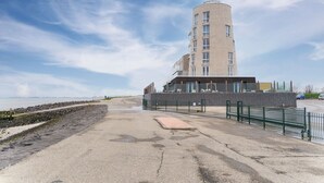 A modern building with a curved facade, a flat roof, and a large glass window section. - Beautiful apartment with sea view (Scherpenisse)