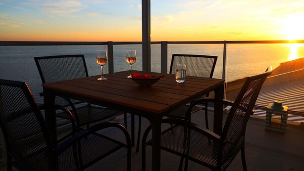 A table with two glasses of wine and a bowl, set against a sunset view. - Beautiful apartment with sea view (Scherpenisse)