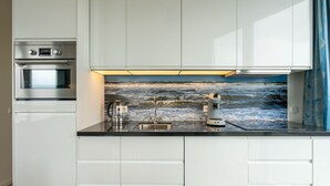 A modern kitchen with white cabinetry, a built-in oven, a stainless steel range hood, and a backsplash with a wave pattern. - Beautiful apartment with sea view (Scherpenisse)