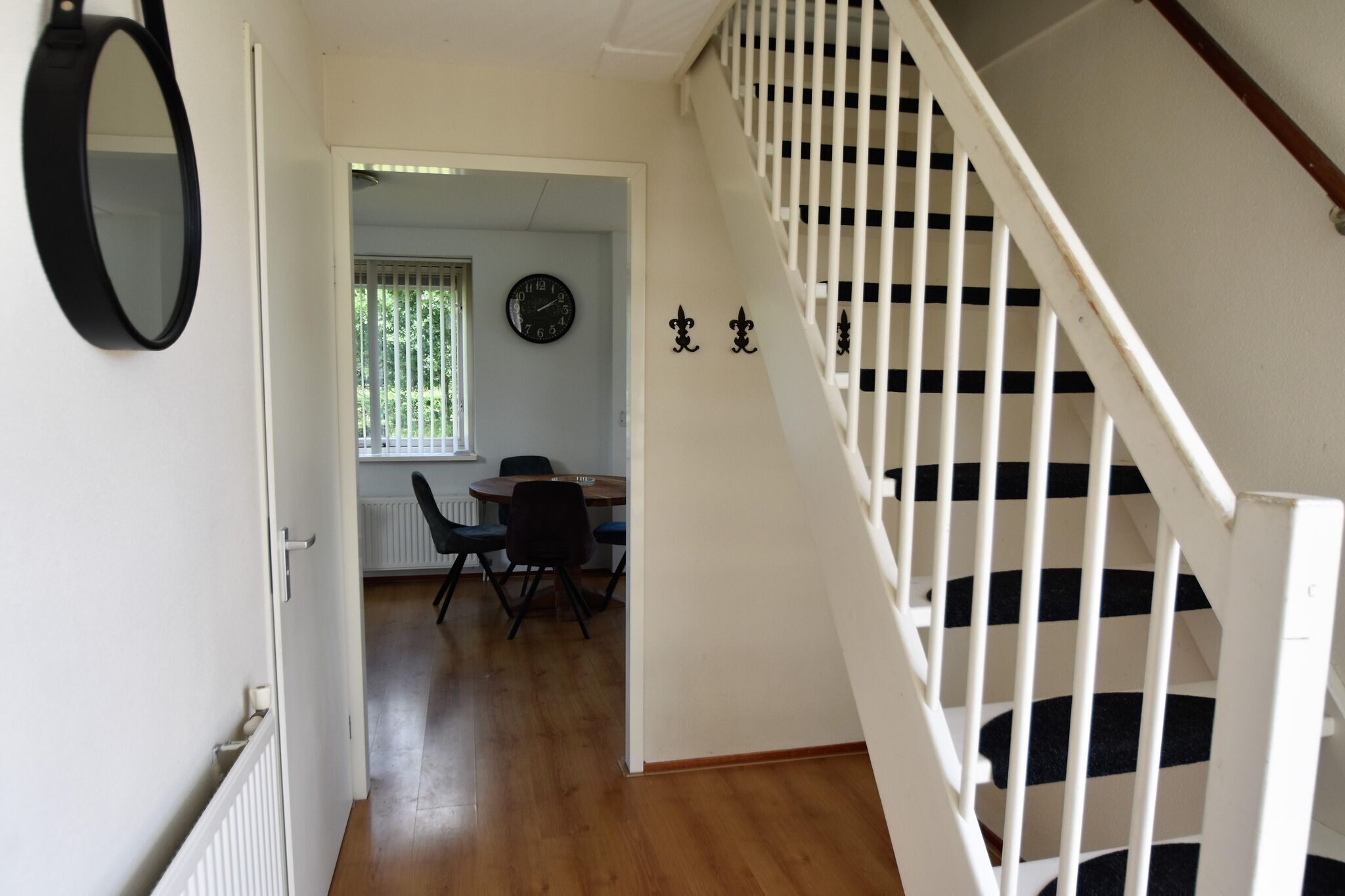 A staircase with white railings and black stripes, leading to an upper floor. A dining area with a table and chairs is visible in the background.