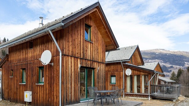 En stuga byggd av trä med en veranda, en satellitmottagare och utsikt över bergen.
