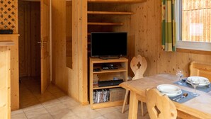 En inredning med träpanel, en tv placerad på en hylla, ett matbord med tallrikar och glas, och ett fönster med gardiner.