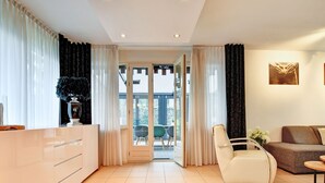 A modern living room with a sofa, a chair, and a dining area with a table and chairs. - Charming holiday home with a covered terrace (Meijel)