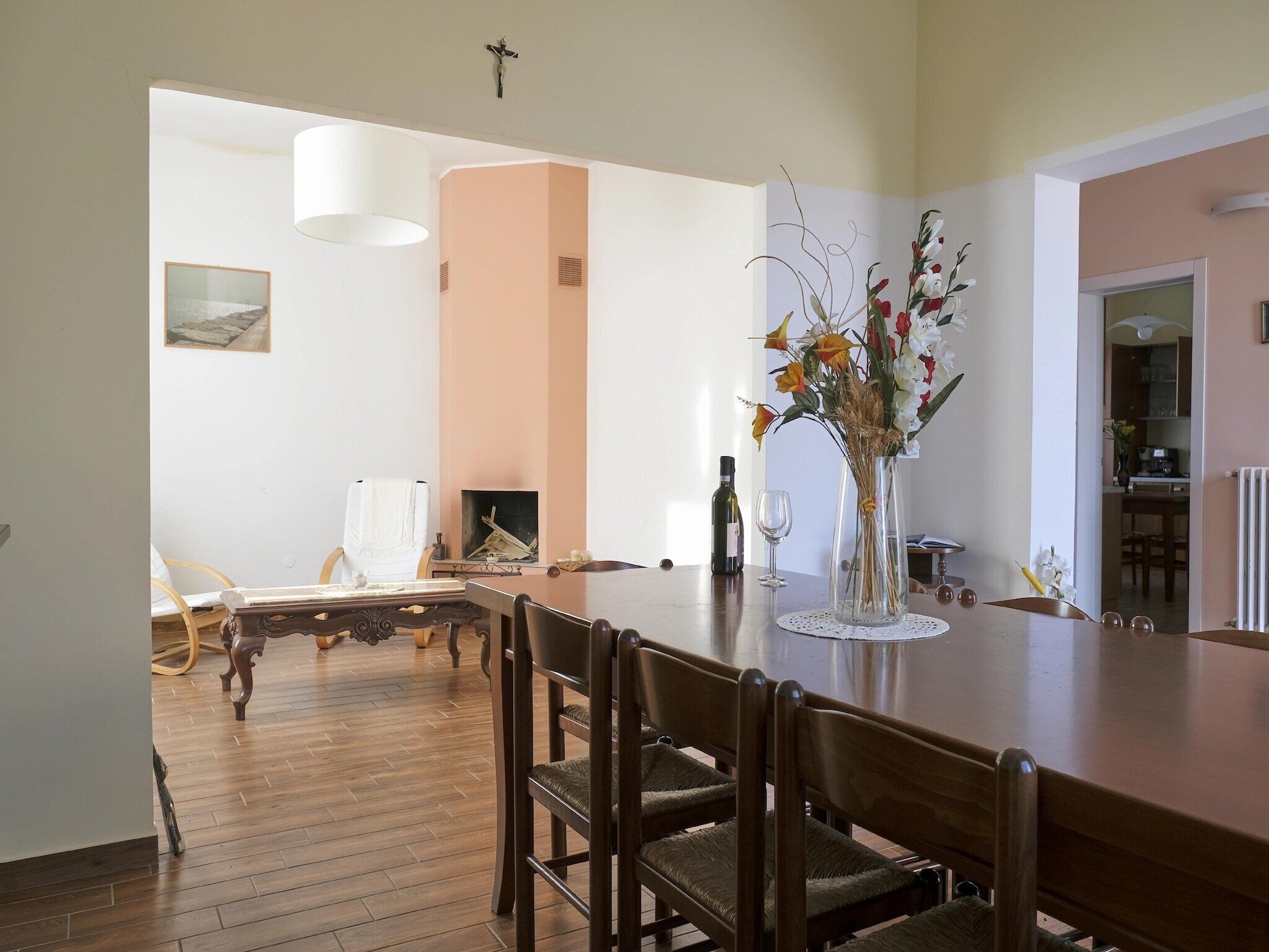 Un coin repas avec une table et des chaises en bois, un vase de fleurs et une croix accrochée au mur.