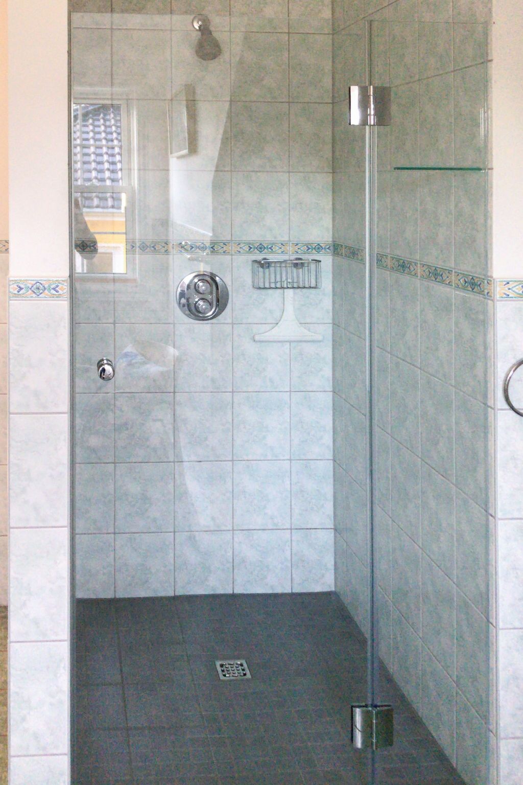 A shower area with a glass door, a hand dryer, and a towel rack.