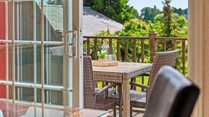 Un balcone con mobili in vimini, un tavolo con una bottiglia e dei bicchieri, e vista su piante.