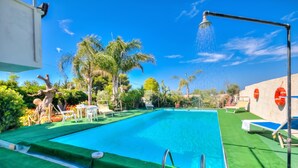 A swimming pool with a shower, surrounded by palm trees and lounge chairs.