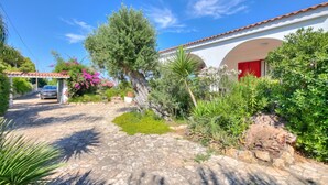 A house with a stone pathway, a red door, and lush greenery.