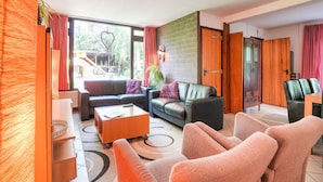 Ein modernes Wohnzimmer mit einer Couch, Sesseln und einem Couchtisch. Eine Ziegelwand und eine Holztür sind ebenfalls vorhanden.