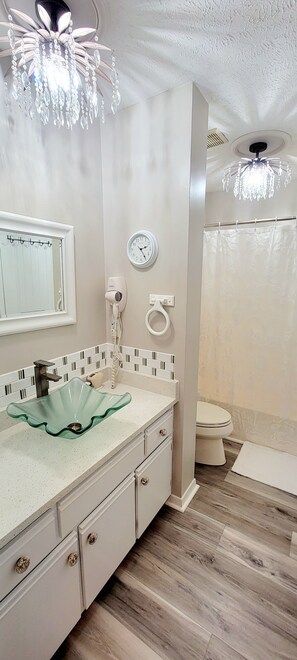 Une salle de bain avec un lavabo en verre, une horloge, un sèche-cheveux et un rideau de douche.
