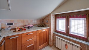 A kitchen with wooden cabinets, a countertop, and a window with a red frame. - Studio Placide Mountain View, Sauze d'Oulx, Italy (Sauze d'Oulx)