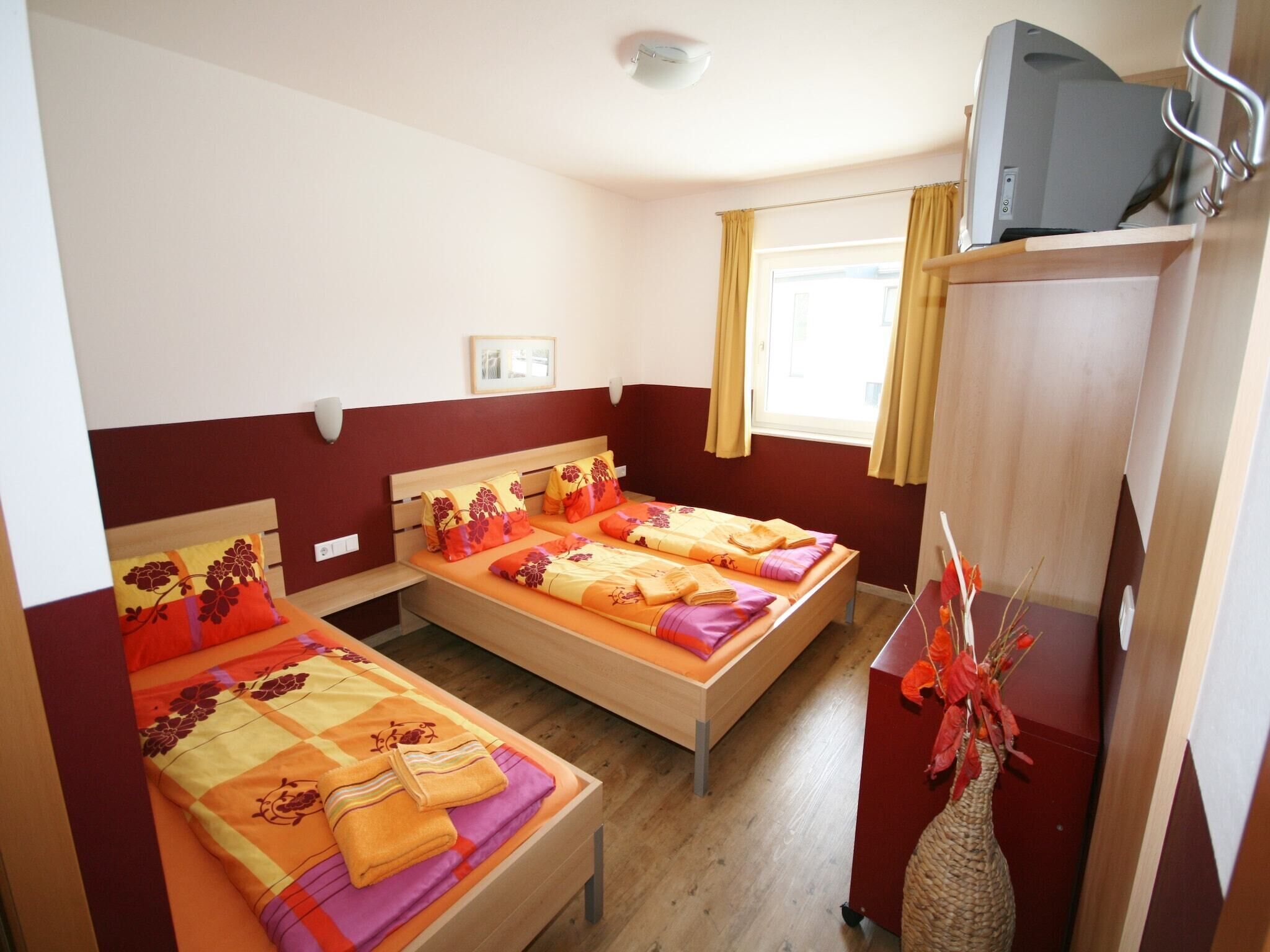 Quarto de hotel com duas camas de solteiro, um guarda-roupa de madeira, uma televisão em cima e uma janela com cortinas.