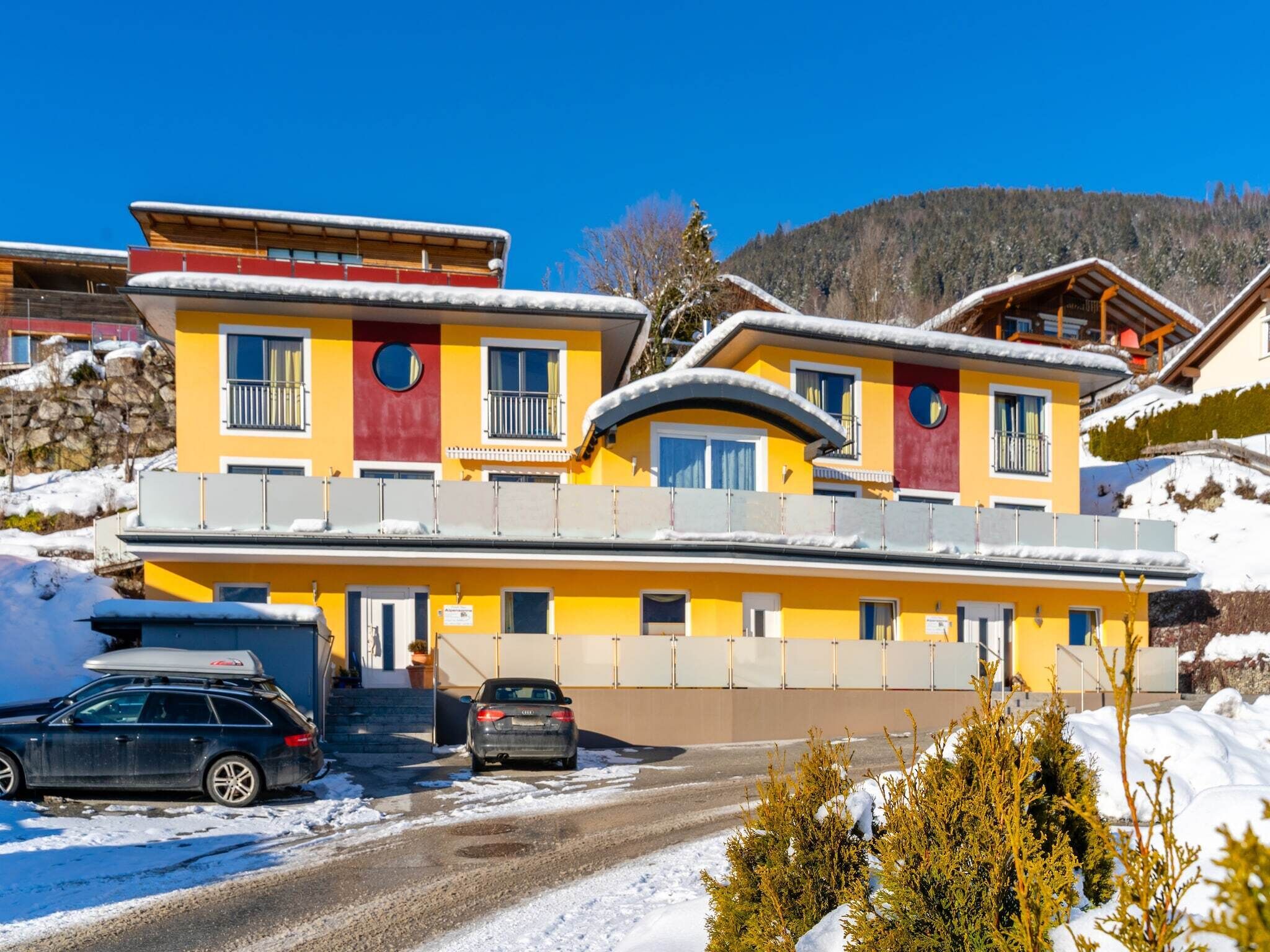 A multi-story hotel with a yellow facade, balconies, and a ski slope in the background.