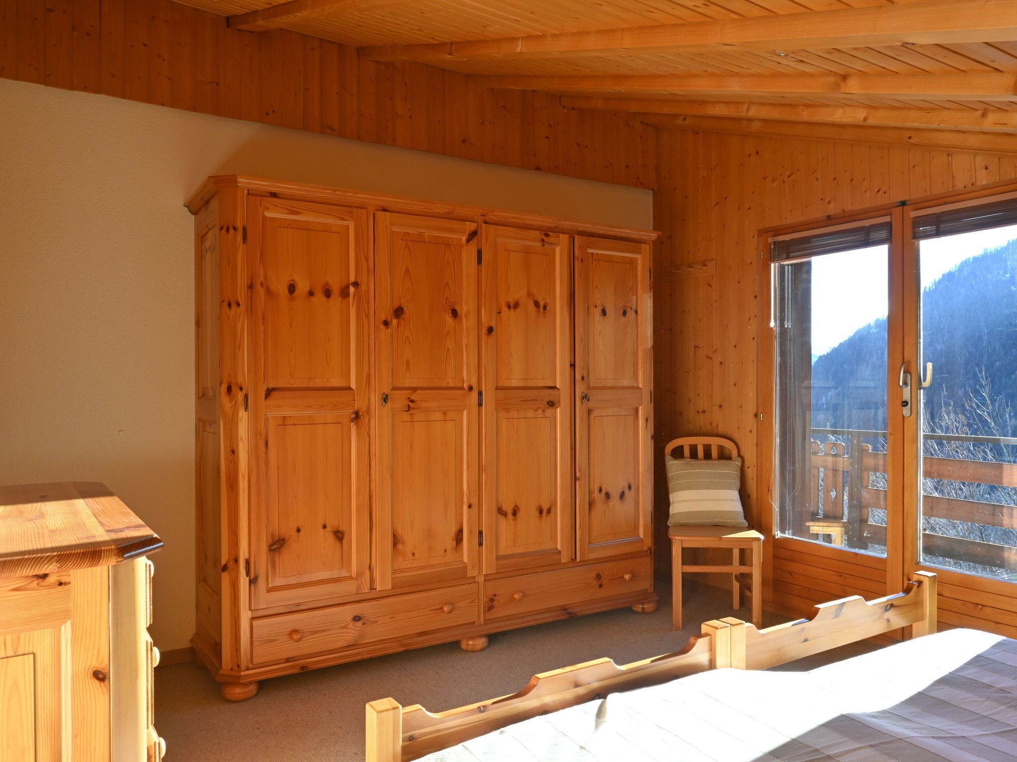 Une pièce en bois avec une grande armoire, un lit et une fenêtre donnant sur les montagnes.