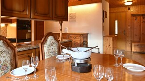 A wooden interior with a dining table set for four, surrounded by wooden cabinets and a kitchen area with modern appliances. - Tourbillon B 31 by Interhome (Ovronnaz)