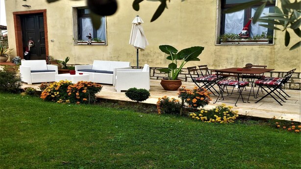 Ein Sitzbereich im Freien mit weißen Korbmöbeln, einem Topf mit Pflanze und einem Tisch mit Stühlen.