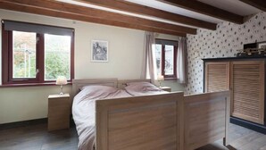 Une chambre à coucher avec un lit en bois, deux fenêtres avec des rideaux, une table de chevet et une armoire.