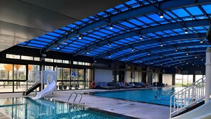 An indoor swimming pool with a glass ceiling, slides, and lounge chairs. - Vinhomes Metropolis Ha Noi-Gem Apartment (Hanoi)