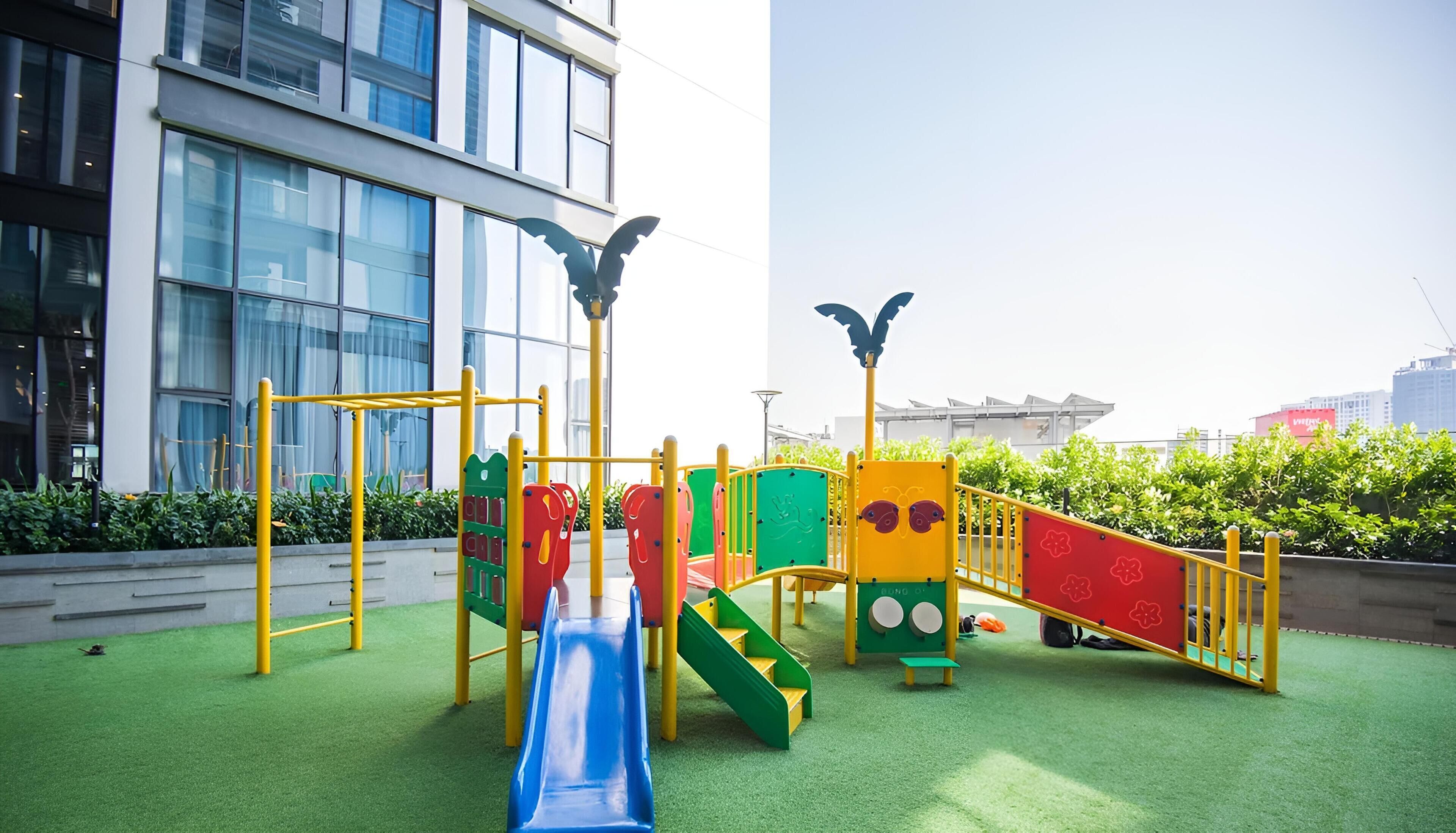 A playground with slides and climbing structures, surrounded by a building with large windows and a clear sky.