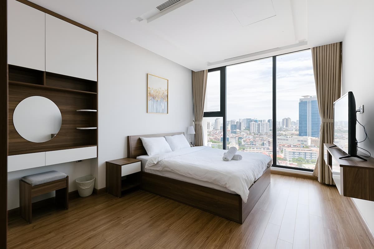 A modern hotel room with a large bed, a TV, a desk, and a view of the city.
