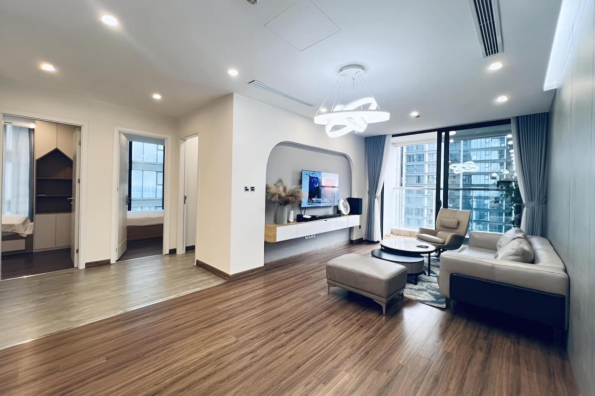 A modern living room with a TV, sofa, and ottoman. There is a wooden floor and a large window with curtains.