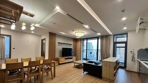 A modern living room with a dining area, a TV, and a kitchen. - Vinhomes Metropolis Ha Noi-Gem Apartment (Hanoi)