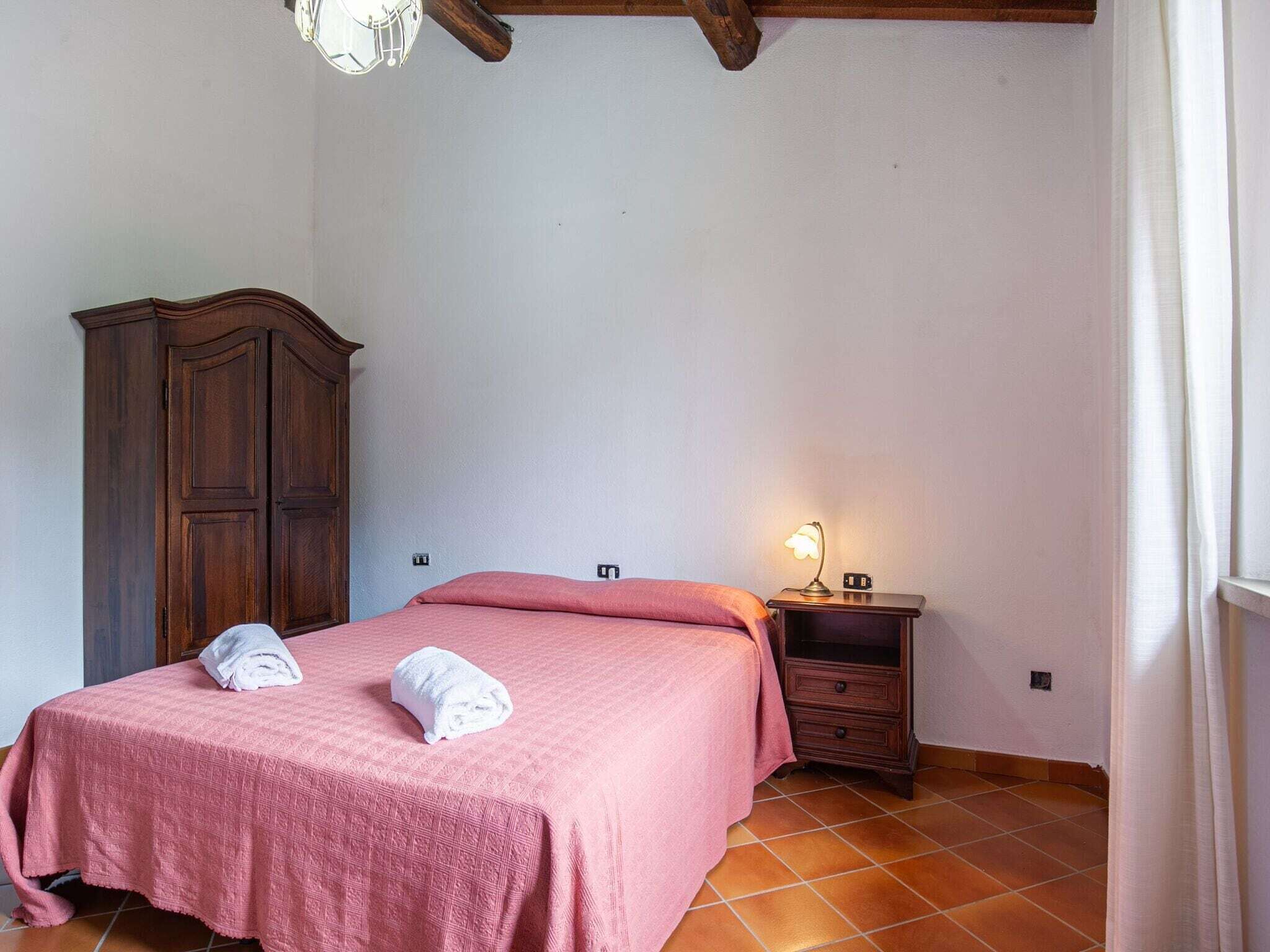 Een slaapkamer met een bed, een houten garderobe, een nachtkastje met een lamp en een betegelde vloer.