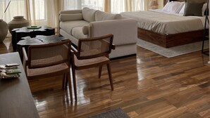 Amplia habitación con una cama grande, un sofá, una mesa de comedor y una silla. Hay un lámpara colgante y un equipo de aire acondicionado en la pared.