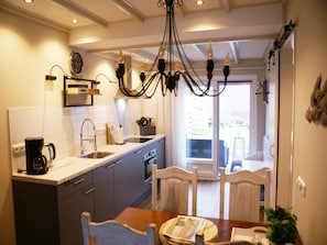 Ett modernt kök med matplats, utrustat med en kristallkrona, en kaffebryggare och ett matbord med stolar.