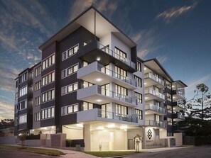 Un hotel de varios pisos con balcones, un logotipo visible y una entrada bien iluminada.