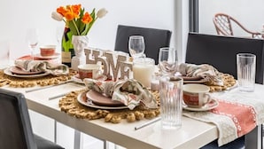 Ein Essbereich mit einem Tisch, gedeckt für vier Personen, mit einer Tulpenvase, einer Kerze und einem Glas Wasser.