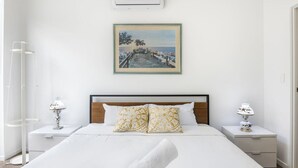 Ein ordentlich eingerichtetes Hotelzimmer mit einem großen Bett, zwei Nachttischen mit Lampen, einem gerahmten Bild an der Wand und einer weißen Klimaanlage über dem Bett.