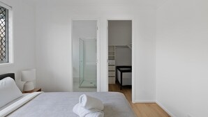 A hotel room with a bed, a nightstand, a lamp, a towel, a glass shower, and a closet. - Brand-new 4BR modern family home @Park Ridge (Park Ridge)