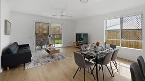 A modern living room with a black sofa, dining table set for four, and a TV in the background. - Brand-new 4BR modern family home @Park Ridge (Park Ridge)